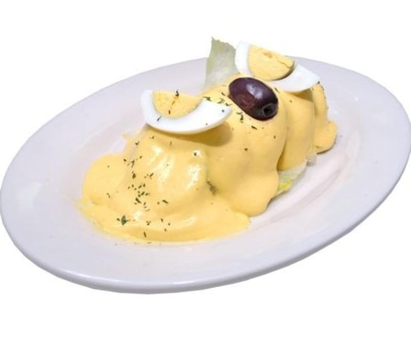 Peruvian Papa a la Huancaína, potatoes covered in yellow cheese sauce, garnished with egg and olive.