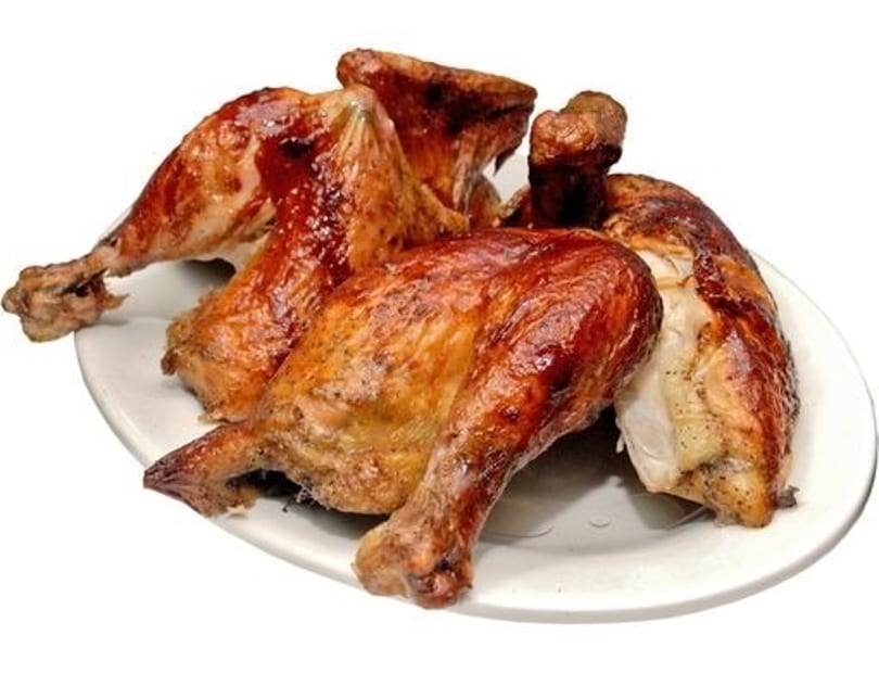 A white plate holds several pieces of golden-brown roasted chicken with crispy skin.
