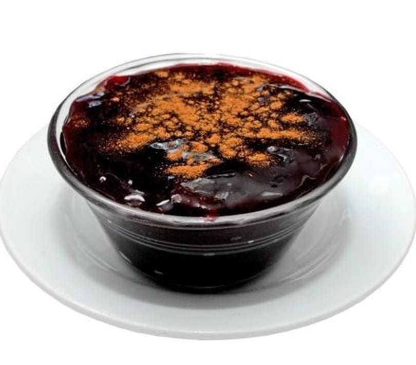 A glass bowl of deep purple mazamorra morada, a Peruvian dessert, topped with cinnamon.
